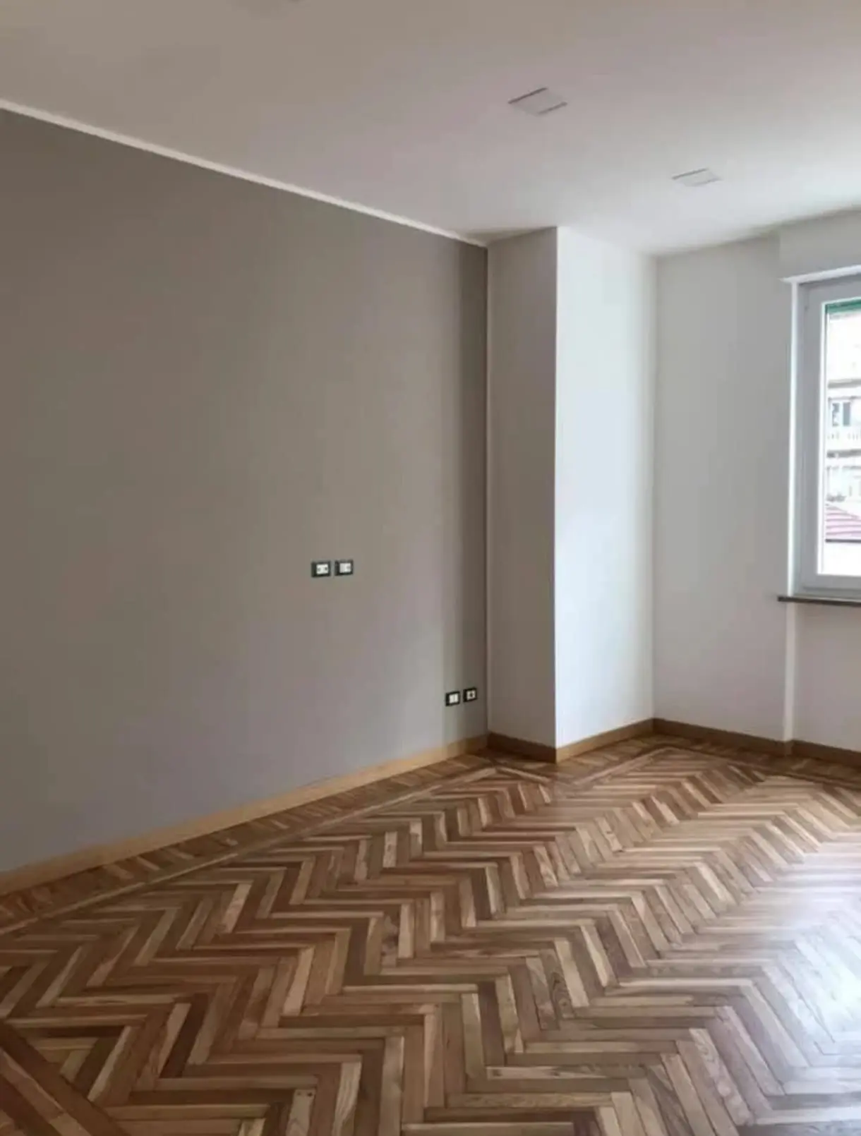 Sala con pared gris y suelo de parquet en espiga